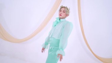 Geniş yay ve kabarık kollu nane yeşili bir elbise giyen, yumuşak, açık renkli kumaşlı bir arka plana poz veren bir manken..