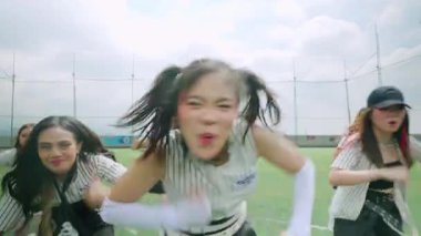 Bulutlu bir gökyüzünün altında yeşil bir alanda gösteri yapan dört dansçı grubu. Şık kıyafetler giyiyorlar ve dans yeteneklerini sergiliyorlar..