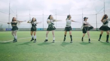 Altı dansçıdan oluşan bir grup, çevreleyen ağlarla çevrili yeşil bir çim sahasında koreografik bir gösteri sergiliyor. Şık siyah beyaz kıyafetler giymişler. Bulutlu bir gökyüzü altında enerjik hareketler sergiliyorlar..