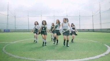 Beş dansçıdan oluşan bir grup yeşil bir spor sahasında koreografi gösterisi yapıyor. Şık kıyafetler giyiyorlar, bulutlu gökyüzüne karşı senkronize hareketler sergiliyorlar..