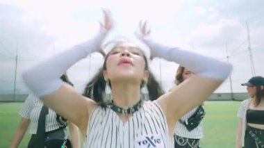 Spor sahasında bir grup dansçı, çizgili şık kıyafetler giyiyorlar. Baş dansçı kendinden emin bir şekilde ön planda duruyor, canlı ve enerjik bir atmosfer sergiliyor..