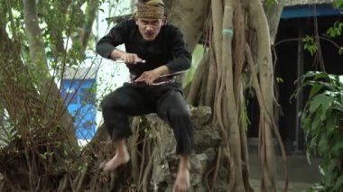 Geleneksel kıyafetli bir dövüş sanatçısı ağaçlar ve yeşilliklerle çevrili açık havada bir duruş sergiler. Pratisyen hekimin şekli ve tekniği üzerinde duruluyor..