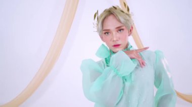 Bir model zarif bir şekilde nane yeşili bir elbiseyle poz verir. Saf kollu, çiçekli bir taçla süslenmiş. Arka plan hafifçe aydınlatılmış, manevi titreşimi arttırıyor..