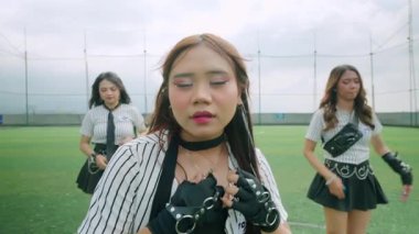 Yeşil bir sahada canlı bir dans gösterisi, şık giyinmiş neşeli bir ifadeyle genç bir kadın. Etrafı dansçılarla çevrili, benzer giyinmiş, enerjik hareketler sergiliyor..