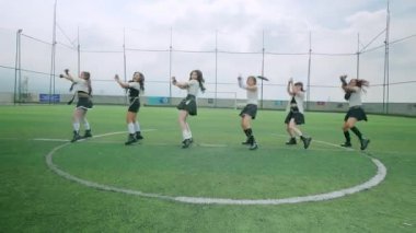 Bir futbol sahasında dinamik bir dans gösterisi. Dört dansçı şık kıyafetler giyecek. Sahne bulutlu bir gökyüzü altında hareket ve enerji yakalar..