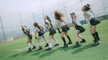 Altı kadından oluşan bir grup çimenli bir alanda dans gösterisi yapıyor. Zincirli şık kıyafetler giyiyorlar. Sahne parlak ve enerjik, canlı bir atmosferi yakalıyor..