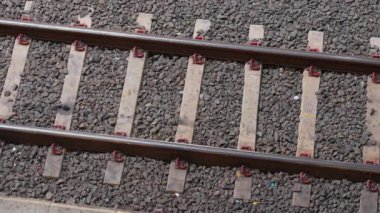 Demiryolu raylarının ahşap yataklı ve çakıllı yakın görüntüsü. Metal raylar kırmızı raptiyelerle korunuyor, tren hattının altyapısını gösteriyor..