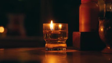 Cam tutacağında yanan bir mum, karanlık bir yüzeye sıcak bir ışık saçıyor. Mum yumuşak yansımalar ve gölgelerle çevrili, rahat bir atmosfer yaratıyor..