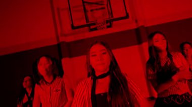 Bir grup dansçı, kırmızı ışıkla aydınlatılmış bir spor salonunda gösteri yapıyor. Dansçılar şık kıyafetler giyer ve kareografilerini sergileyerek enerjik hareketler sergilerler..