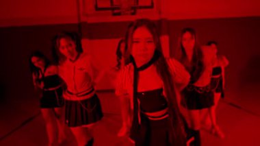 Kırmızı ışıklı bir spor salonundaki dinamik dans gösterisi, şık kıyafetler içinde birden fazla dansçının yer aldığı. Atmosfer enerjik ve canlı, hareketi ve ritmi yakalıyor..