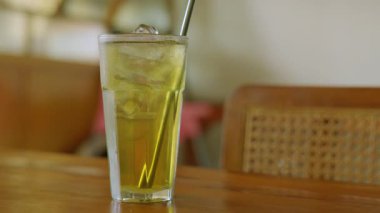 Sıcak bir ortamda ahşap bir masanın üzerine buz küpleri ve pipetle serinletici bir bardak buzlu yeşil çay..