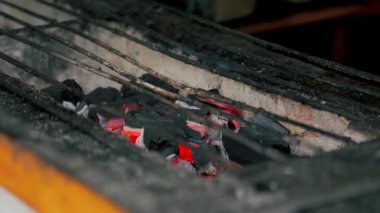 Izgarada, kül ve metal ızgaralarla parlayan kömürün yakın çekimi. Közler kırmızı ve sıcak. Yemek yapmaya hazır olduklarını gösteriyor..