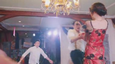 Ön planda bulanık bir figür ve arka planda dans eden bir çift. Dekoratif perdeler ve ahşap fıçılar içeriyor ve şenlikli bir atmosfer yaratıyor..