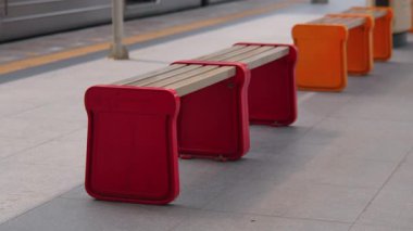 Modern bir tren istasyonunda renkli banklar, kırmızı ve turuncu tasarımlar, parlak, minimalist estetik.