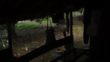 Dışarıdan yağan yağmuru gösteren bir kır evi manzarası. Sahne yeşillik ve toprak zemin ile doğal bir ortam yakalıyor, dingin bir atmosfer yaratıyor..