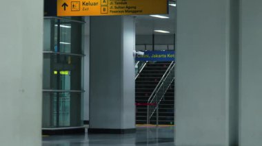 Çıkışlar ve sokak isimleri için açık tabelalar bulunan modern bir ulaşım istasyonunun iç görünümü. Mimaride cam paneller ve merdivenler var, geniş bir atmosfer yaratıyorlar..