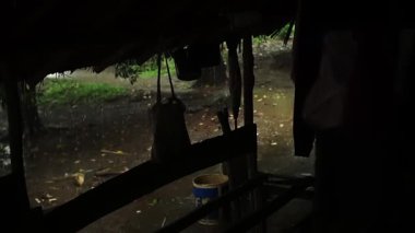 Barınağın içinden dışarıdan yağmurun yağdığını gösteren kırsal bir manzara. Olay yeri yeşillik ve toprak zeminli doğal bir ortam yakalıyor ve sakin bir atmosfer yaratıyor..