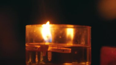 İçi sıvı dolu bir cam kabın içinde yanıp sönen bir mum alevi. Sıvının yüzeyinde süzülen ahşap bir mandal huzurlu ve sıcak bir atmosfer yaratıyor..