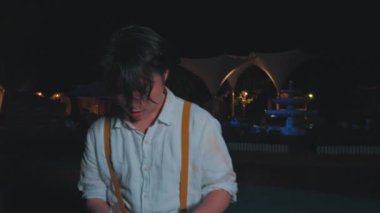 Uzun saçlı, beyaz gömlekli ve pantolon askısı takan genç bir adam gece hareket ediyor gibi görünüyor. İfadesi çok yoğun, dramatik bir an olduğunu gösteriyor..