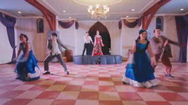 Kareli bir katta dört renkli kostümlü dansçının olduğu canlı bir dans gösterisi. Dekorasyon, avizesi ve perdeleri olan süslü bir salon. Şenlikli bir atmosfer yaratıyor..