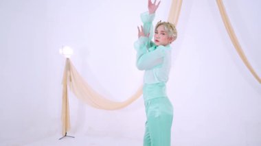 Nane yeşili kıyafetli bir dansçı arka planda yumuşak örtülü kumaşla minimalist bir stüdyo ortamında gösteri yapar..