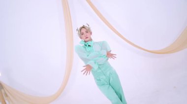 Zarif bir şahıs, minimalist beyaz bir arkaplana karşı yeşil bir elbiseyle poz verir. Kumaşın yumuşak perdeleri sahneye biraz zarafet katar..