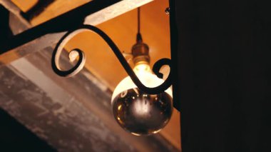 Dekoratif metal bir desteğe asılı yuvarlak cam bir ampulle klasik tarzda bir lamba. Işığın sıcak parıltısı çevreyi aydınlatır ve rahat bir atmosfer yaratır..