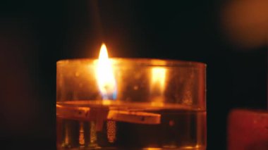 İçi sıvı dolu bir cam kabın içinde yanıp sönen bir mum alevi. Alevin sıcak parıltısı camdan yansıyarak sakin ve rahatlatıcı bir atmosfer yaratır..