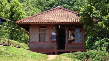 Yeşilliklerle çevrili, eğimli çatılı geleneksel bir ahşap ev. Ev, bir veranda ve kırsal alanda geçen ahşap pencerelere sahip..