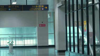 Büyük camlı pencereli ve platform numaralarını gösteren bir tabela olan kapalı bir tren istasyonu alanı. Zemin parlak ve çevreyi yansıtıyor, modern bir atmosfer yaratıyor..