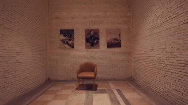 Merkezde tek bir sandalyenin olduğu, dokulu beyaz tuğla duvarlarla çevrili minimalist bir iç mekan. Duvarda asılı duran üç çerçeveli fotoğraf, uzaya sanatsal bir dokunuş ekliyor..