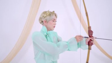 Nane yeşili kıyafetli, ok ve yayla ateş etmeye hazır biri. Hassas bir taç giyiyorlar ve yumuşak, tarafsız bir arkaplana karşı odaklanmış bir ifadeleri var..