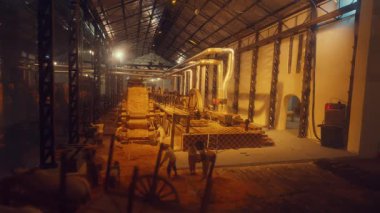 Büyük, iyi ışıklandırılmış bir alanda tarihi makine ve aletlerin sergilendiği bir endüstri müzesi. Sahne çeşitli ekipmanları, ahşap arabaları ve üretimin geçmişini yansıtan tozlu zemini içeriyor..