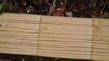 Ahşap bir kalasın oyulduğu ya da bir aletle şekillendirildiği, detaylı ahşap talaşlarını ve dokularını gösteren yakın çekim görüntüsü. Arkaplanda biraz yeşillik ve enkaz var..