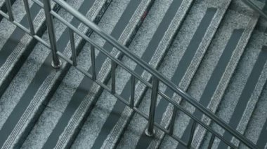 Metal parmaklıklı bir merdivenin yakın çekim görüntüsü. Merdivenler beyaz çizgili gri taştan yapılmış modern ve parlak bir görünüm yaratıyor. Perspektif, parmaklıkları ve basamakların dokusunu yakalar..