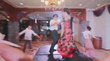 Canlı kostümler giymiş iki dansçının sahne aldığı bir tiyatro gösterisi. Kadın dansçı kırmızı ve siyah bir elbise giyer, erkek dansçı ise beyaz gömlek ve siyah pantolon giyer. Arka planda diğer sanatçılar kollarını kaldırıyorlar.