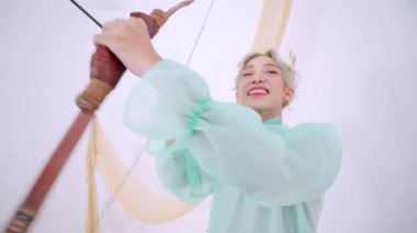 Açık yeşil kıyafetli bir kişi yaylı bir oku hedef alıyor, odaklanma ve kararlılık gösteriyor. Arka plan minimalistik, deneğin ifadesini ve duruşunu geliştiriyor..