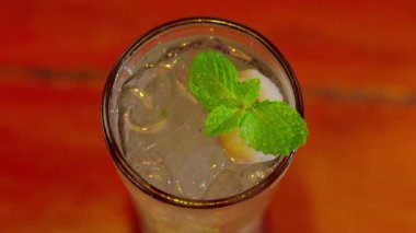 Buzla dolu, taze nane yapraklarıyla süslenmiş uzun bir bardakta servis edilen ferahlatıcı bir içecek. İçki berrak ve köpüklü görünüyor. Kokteyl ya da soda olabilir..