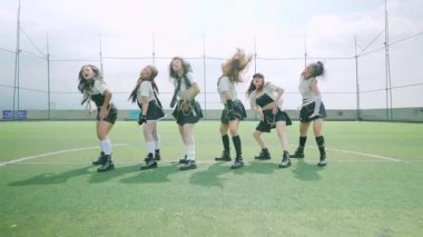 Altı kadın dansçıdan oluşan bir grup yeşil bir çim sahasında koreografili bir gösteri yapıyor. Parlak gökyüzüne karşı siyah-beyaz, dinamik pozlar veren şık kıyafetler giyiyorlar..