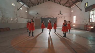 Bir grup kırmızı elbiseli dansçı boş bir endüstriyel alanda gösteri yapıyorlar. Dansçılar çeşitli pozlarda, koreografilerini sergiliyorlar. Ayarda yüksek tavanlar ve geniş pencereler yer alıyor ve dramatik bir atmosfer yaratıyor..