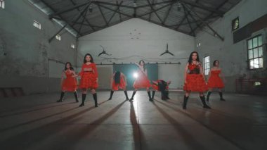 Bir grup kırmızı elbiseli dansçı endüstriyel alanda gösteri yapıyorlar. Dansçılar senkronize, dinamik hareketler ve ifadeler sergiliyorlar. Mekanın kırsal ve geniş bir havası var. Yüksek tavanları ve küçük dekorları var..