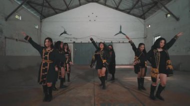 Bir grup dansçı, sanayi bölgesinde yüksek tavanlı ve asgari dekorlu senkronize bir gösteri yapıyorlar. Dansçılar dinamik bir pozda, yeteneklerini ve takım çalışmalarını sergiliyorlar..