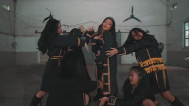 Bir grup dansçı endüstriyel alanda dinamik bir gösteri yapıyorlar. Altın aksanlı koyu kıyafetler giyiyorlar, dışavurumcu hareketler sergiliyorlar. Atmosfer enerjik ve sanatsal..