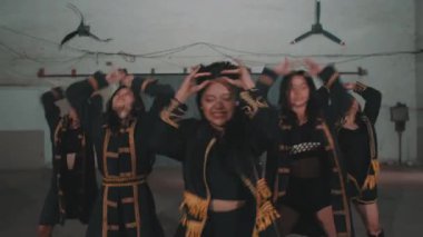 Bir grup dansçı endüstriyel bir alanda koreografi gösterisi yapıyor. Altın aksanlı siyah kıyafetler giyiyorlar, dinamik hareketler ve ifadeler sergiliyorlar..