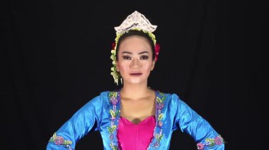 Geleneksel kıyafetli bir sanatçı. Karmaşık tasarımları ve dekoratif başlığı olan canlı bir mavi kostüm. Arka plan siyah, renkli kıyafetleri ve makyajı vurguluyor..