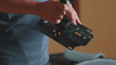 Elinde siyah metal parçası olan bir kişi, muhtemelen bir makine ya da mobilya parçası. Arkaplan bulanık, elindeki nesneye odaklanıyor.