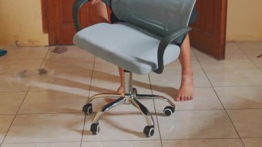 Ofis sandalyesini monte eden, koltuk yüksekliğini sandalyeyle ayarlayan biri. Yerler fayanslarla döşenmiş ve arka planda ahşap kapılar var..