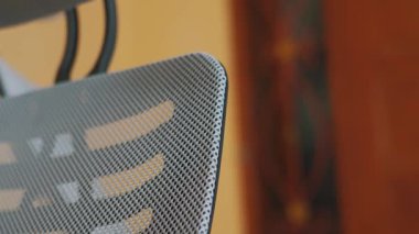 Modern bir ofis sandalyesinin arka planına yakın plan, ergonomik özelliklerini ve parlak çizgilerini yumuşak bulanık bir arkaplana karşı sergiliyor..