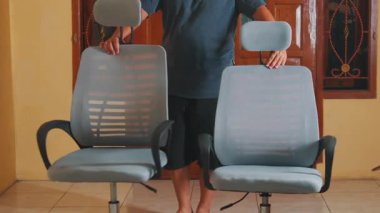 Sarı duvarlı ve ahşap pencereli bir odada iki modern ofis sandalyesini ayarlayan biri. Sandalyeler örgü sırtlı ve ayarlanabilir başlıklı ergonomik..