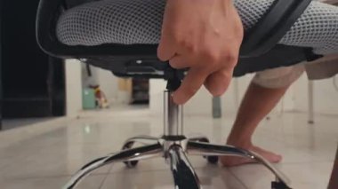 Bir kişinin çıplak ayağının yerde dinlendiği bir ofis sandalyesinin yakın çekim görüntüsü. Arka planda açık renkli duvarları ve en az dekorasyonu olan basit bir oda var..